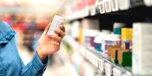 close up of hand holding pill bottle in a pharmacy isle